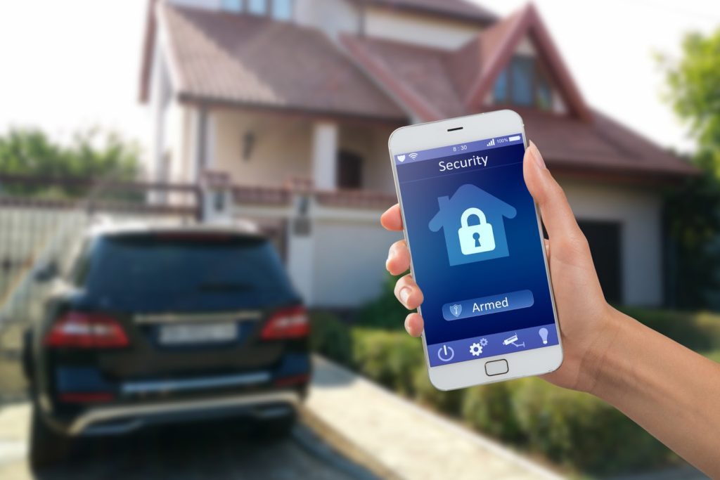 Smartphone with home security app in a hand with home in the background
